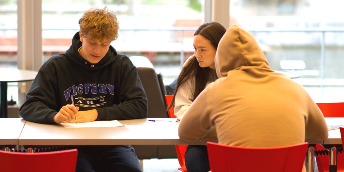 Studerende, der sidder ved et bord og arbejder sammen om at skrive noter