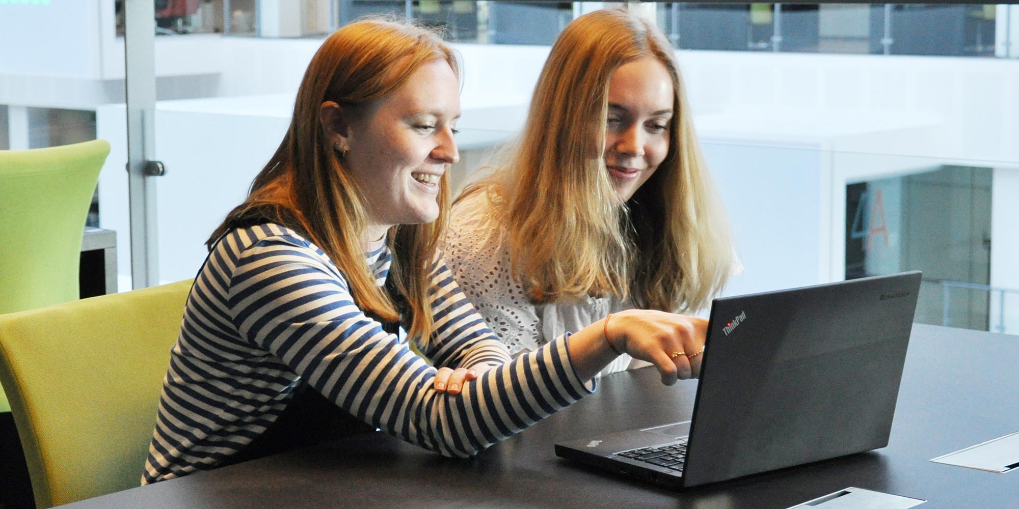 Two female students at table, looking at a laptop
